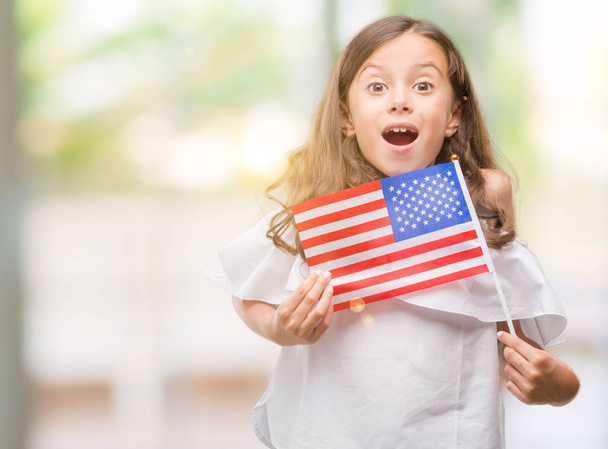 Brunette-Spaanse meisje vlag van Verenigde Staten bang in schok met een verrassing gezicht, bang en opgewonden met angst expressie te houden - Foto, afbeelding