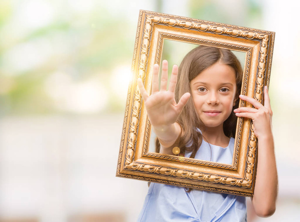 Брюнетка латиноамериканського дівчина Холдинг vintage мистецтва рамка з відкриті боку робити знак зупинки з серйозним і впевненим вираз, жест оборони - Фото, зображення