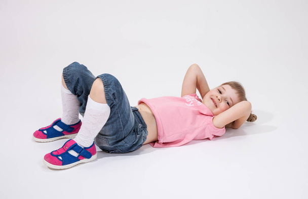 Smiling little girl lying on the floor; white background - 写真・画像