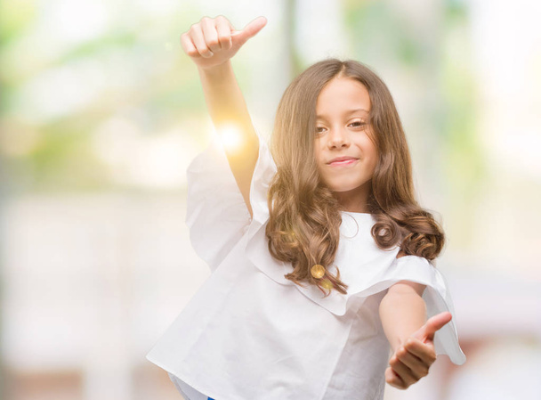 Brunette hispanic girl approving doing positive gesture with hand, thumbs up smiling and happy for success. Looking at the camera, winner gesture. - 写真・画像