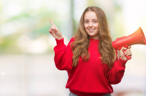Jeune femme blonde tenant mégaphone rouge très heureux pointant avec la main et le doigt sur le côté
 - Photo, image