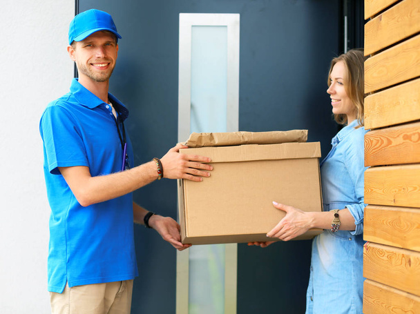 Smiling delivery man in blue uniform delivering parcel box to recipient - courier service concept. Smiling delivery man in blue uniform - Foto, immagini