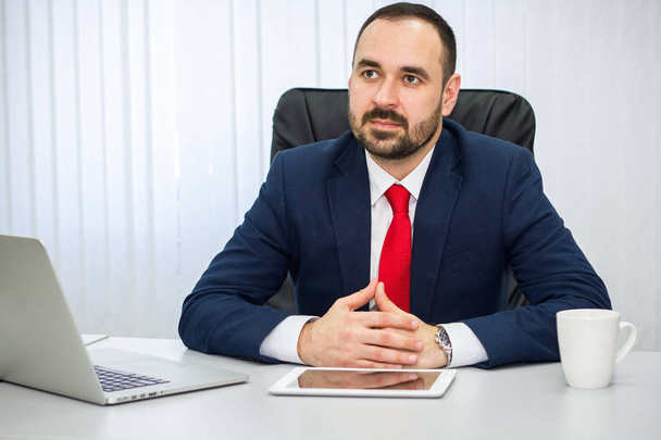 Geschäftsmann in blauem Anzug und roter Krawatte hört seinem Gesprächspartner im Büro aufmerksam zu - Foto, Bild