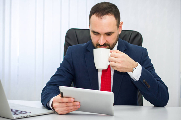 Geschäftsmann in blauem Anzug und roter Krawatte liest Nachrichten auf Tablet - Foto, Bild