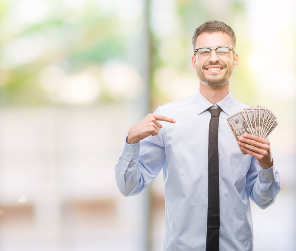 Joven hombre de negocios hipster sosteniendo dólares con la cara sorpresa señalándose a sí mismo
 - Foto, Imagen