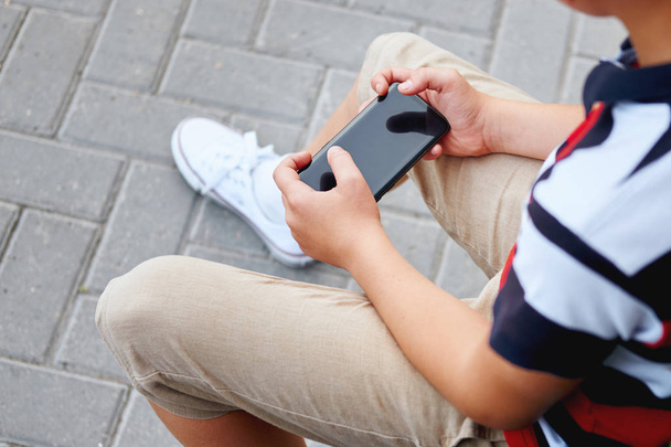 Child sitting outside school and playing games on his cell phone - Φωτογραφία, εικόνα