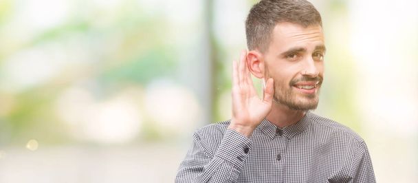 Молодий хіпстер посміхається з рукою через вухо слухаючи слух до чуток або пліток. Концепція глухоти
. - Фото, зображення