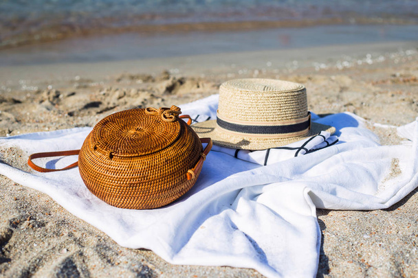 Saco tecido redondo moderno feminino no piso branco na praia ao lado do chapéu e outros acessórios. Coisas para relaxar junto ao conceito do mar
 - Foto, Imagem