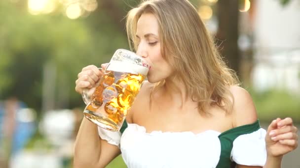 Молодая женщина в традиционном баварском костюме пьет пиво и неловко вытирает пену о губы. Красные губы, сексуально, эротично. Фестиваль музыкального пива Октоберфест
. - Кадры, видео