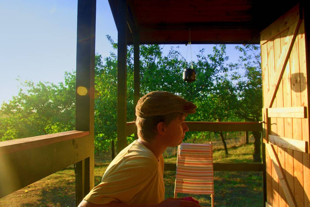 El joven está sentado en una veranda y comiendo manzanas frescas. Imagen onírica y romántica. Verano y concepto de infancia feliz
 - Foto, Imagen
