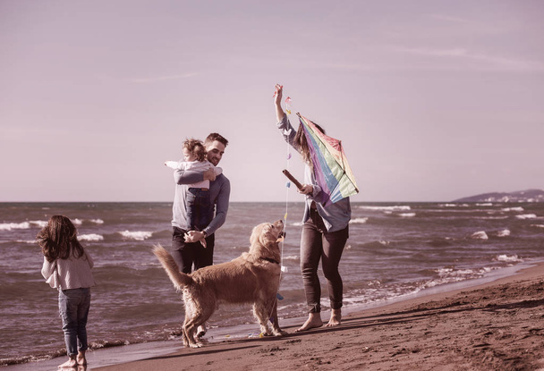 happy young family with kids having fun with a dog and  kite at beach during autumn day filter - Photo, image