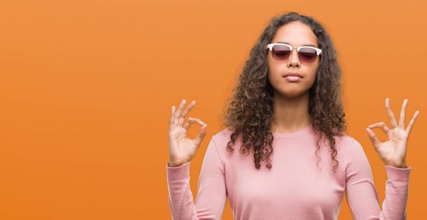 Beautiful young hispanic woman wearing sunglasses relax and smiling with eyes closed doing meditation gesture with fingers. Yoga concept. - Φωτογραφία, εικόνα