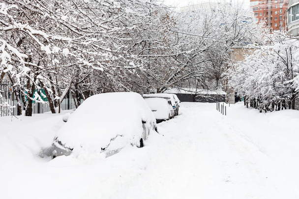 Schneebedeckte Autos auf einem Parkplatz entlang der Straße in einem Wohnviertel der Stadt Moskau an einem trüben Wintertag - Foto, Bild