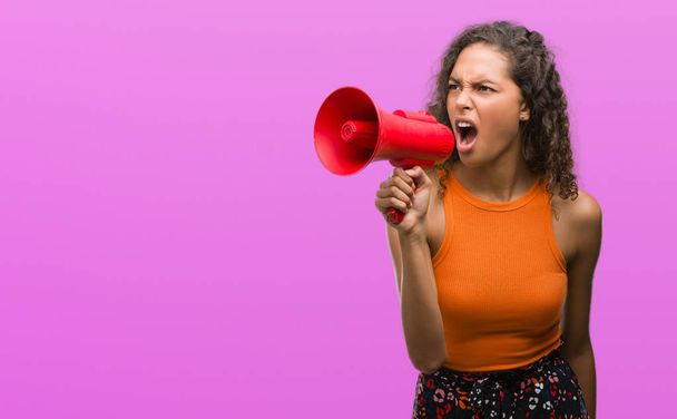 Молода іспаномовна жінка тримає мегафон роздратований і розчарований крик з гнівом, божевіллям і криком з піднятою рукою, концепцією гніву
 - Фото, зображення
