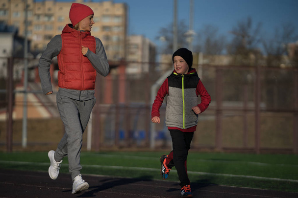 Vrouw en jongen uitvoeren Lopers joggen atletiekbaan. Familie fitness model opleiding buiten - Foto, afbeelding
