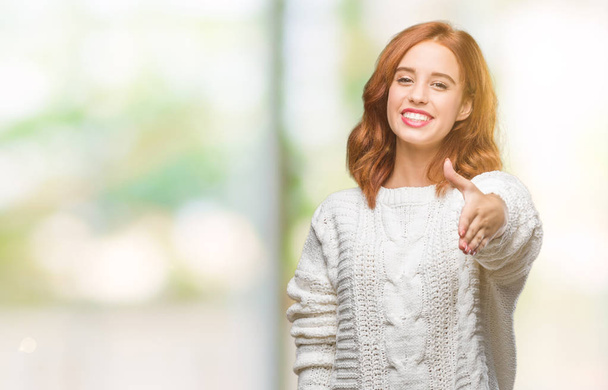 Młoda piękna kobieta na białym tle swetrze zima uśmiechający się oferujący przyjazny uścisk dłoni jako pozdrowienie i przyjazna. Udanego biznesu. - Zdjęcie, obraz