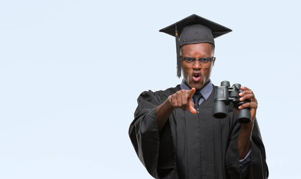 Jovem graduado afro-americano procurando um emprego usando binóculos apontando com o dedo para a câmera e para você, sinal de mão, gesto positivo e confiante da frente
 - Foto, Imagem