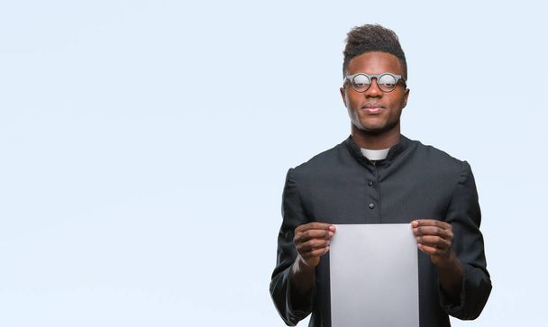 Young african american priest man over isolated background holding blank paper with a confident expression on smart face thinking serious - Photo, Image