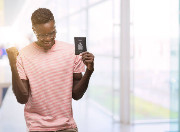 Young african american man holding canadian passport screaming proud and celebrating victory and success very excited, cheering emotion - Foto, imagen