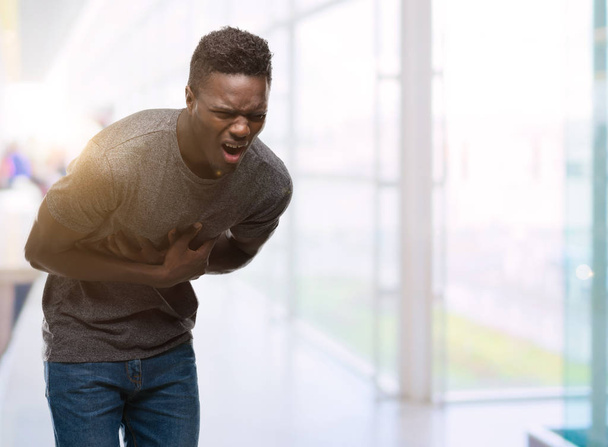 Νεαρός αφρικανική αμερικανική άνθρωπος που φορώντας γκρι t-shirt με το χέρι στο στομάχι, επειδή ναυτία, οδυνηρή ασθένεια αδιαθεσία. Πονούν έννοια. - Φωτογραφία, εικόνα