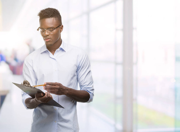 Young african american man holding a clipboarad with a confident expression on smart face thinking serious - Foto, immagini