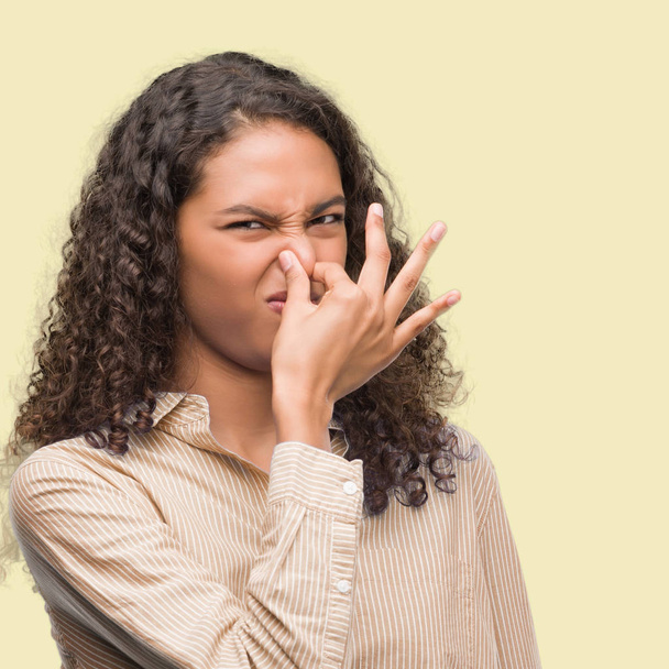 Young hispanic business woman smelling something stinky and disgusting, intolerable smell, holding breath with fingers on nose. Bad smells concept. - Photo, Image