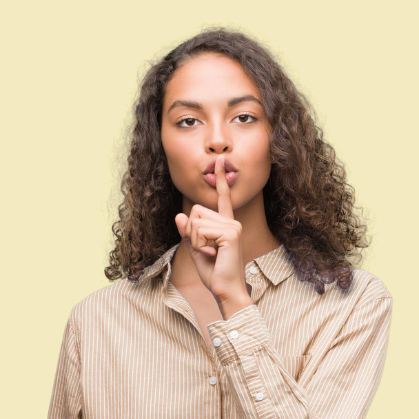 Jeune femme d'affaires hispanique demandant à se taire avec le doigt sur les lèvres. Silence et concept secret
. - Photo, image