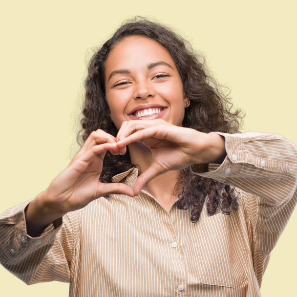 Joven mujer de negocios hispana sonriendo enamorada mostrando el símbolo del corazón y la forma con las manos. Concepto romántico
. - Foto, Imagen