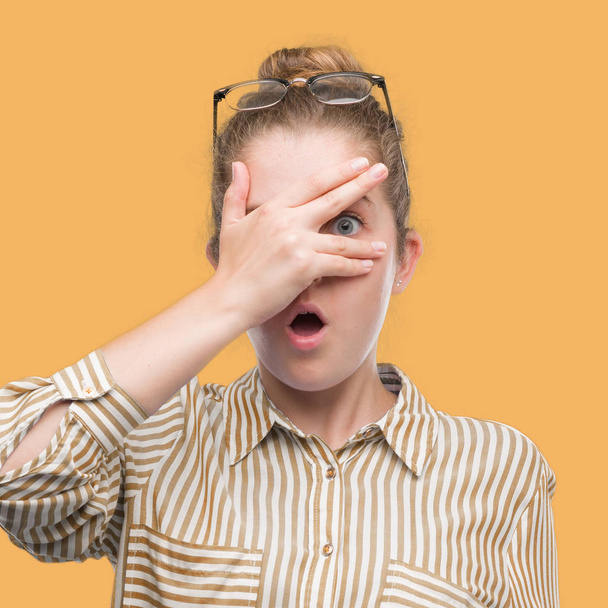 Young blonde business woman peeking in shock covering face and eyes with hand, looking through fingers with embarrassed expression. - Photo, Image