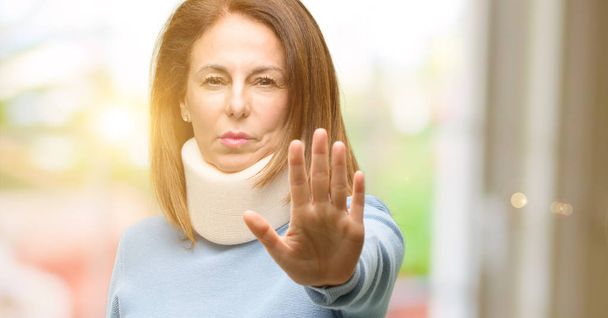 Mujer lesionada con cuello ortopédico molesto con mala actitud haciendo señal de stop con la mano, diciendo que no, expresando seguridad, defensa o restricción, tal vez empujando
 - Foto, imagen