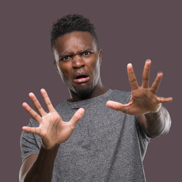 Young african american man wearing grey t-shirt afraid and terrified with fear expression stop gesture with hands, shouting in shock. Panic concept. - Fotoğraf, Görsel