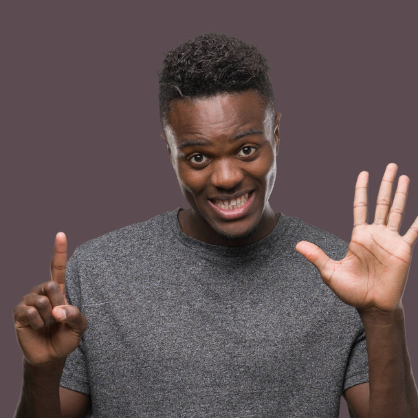 Gösterilen ve parmakları ile işaret gri t-shirt giyen genç Afro-Amerikan adam kendinden emin ve mutlu gülümseyerek süre 6 numara. - Fotoğraf, Görsel
