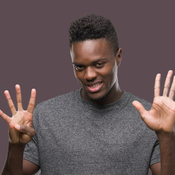 Jonge african american man die grijs t-shirt tonen en met vingers omhoog nummer negen terwijl lacht zelfverzekerd en blij. - Foto, afbeelding