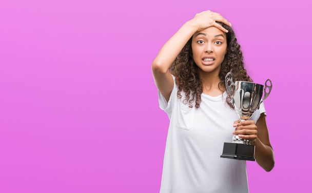 Young hispanic woman holding trophy stressed with hand on head, shocked with shame and surprise face, angry and frustrated. Fear and upset for mistake. - Photo, Image