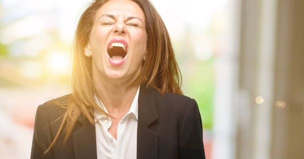 Μέσης ηλικίας γυναίκα που φοράει σακάκι αγχωτικός, τρομαγμένος στον πανικό, φωνάζει εξοργισμένος και απογοητευμένοι. Δυσάρεστη χειρονομία. Ενοχλητικό εργασίας με τρελαίνει - Φωτογραφία, εικόνα