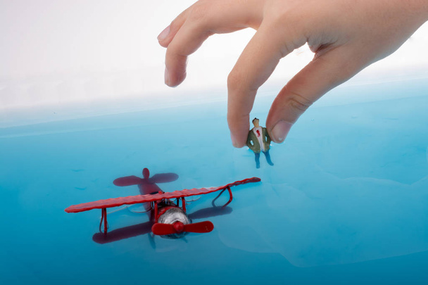 Hand holding a model airplane and a man figurine in blue water - Photo, Image