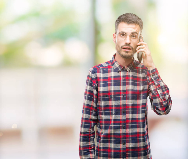 Young hipster adult man talking on the phone scared in shock with a surprise face, afraid and excited with fear expression - Photo, Image