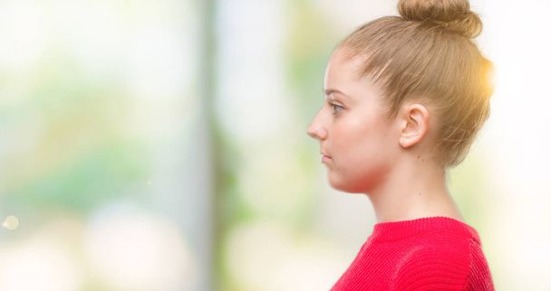 Młoda kobieta blonde noszenie bun i czerwony sweter patrząc w bok, zrelaksować się poza profil z naturalną twarz uśmiech i pewność siebie. - Zdjęcie, obraz