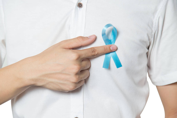 Men's healthcare concept - close up of male hand pointing to light blue ribbon for prostate cancer at left chest isolated on white background. - Foto, imagen