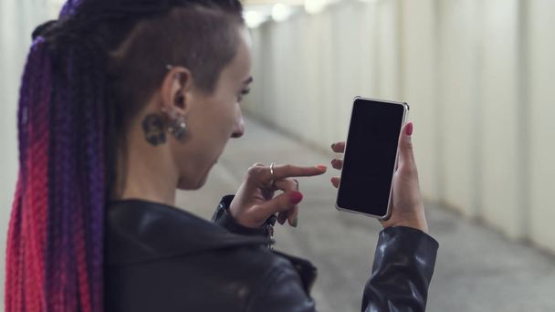 Vrouw op zoek smartphone. sexy mooi meisje met een niet-standaard verschijning luistert naar muziek op de telefoon. Rocker rockandroll - Foto, afbeelding