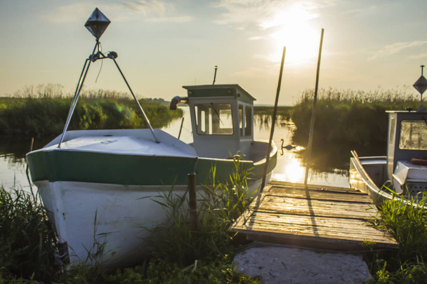 Tôt le matin sur la baie de Vistule. Un bateau de pêche amarré à un petit canot en bois.Roseaux et eau calme. Site sur la nature, mer, pêche, art, fond
. - Photo, image