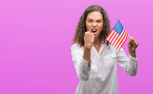 Joven mujer hispana sosteniendo bandera de Estados Unidos de América molesta y frustrada gritando con ira, loca y gritando con la mano levantada, concepto de ira
 - Foto, imagen