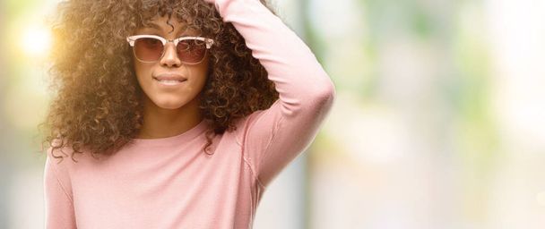 Donna afroamericana con occhiali da sole rosa sorpreso con mano sulla testa per errore, ricordare l'errore. Dimenticato, concetto di cattiva memoria
. - Foto, immagini