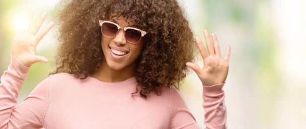 Africká americká žena nosí růžové brýle zobrazující a ukázal prsty desítka, zatímco s úsměvem a spokojené. - Fotografie, Obrázek