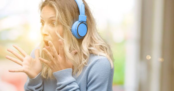 Młoda kobieta piękne słuchanie muzyki stresujące utrzymanie ręce na głowie, przerażony w panice, krzycząc: - Zdjęcie, obraz