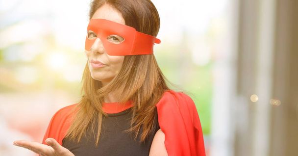 Жінка-супергерой середнього віку в червоній масці і накид тримає щось у порожній руці
 - Фото, зображення