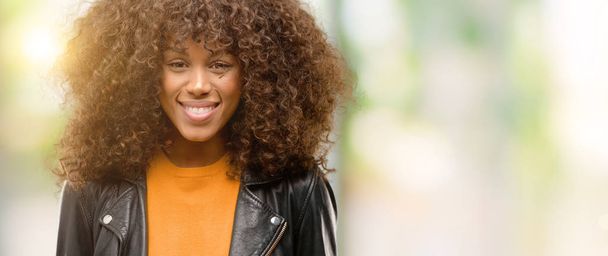 Femme afro-américaine portant une veste en cuir avec un visage heureux debout et souriant avec un sourire confiant montrant les dents
 - Photo, image