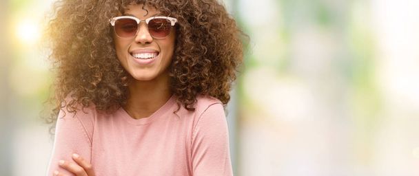 afrikanisch-amerikanische Frau mit rosa Sonnenbrille glücklich lächelnd mit verschränkten Armen in die Kamera blickend. positive Person. - Foto, Bild