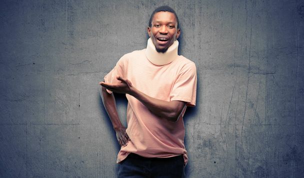 Hombre negro africano lesionado con corsé en el cuello sosteniendo algo en la mano vacía
 - Foto, Imagen