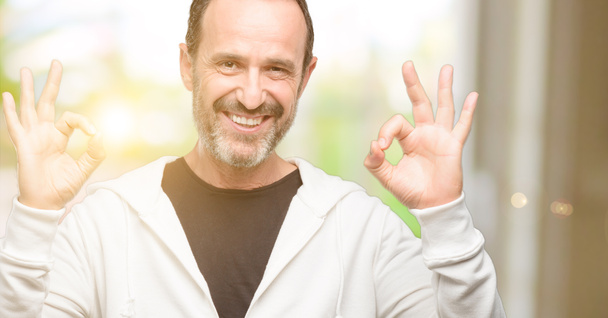 Homme d'âge moyen portant des vêtements de sport faisant signe ok geste avec les deux mains exprimant la méditation et la relaxation
 - Photo, image